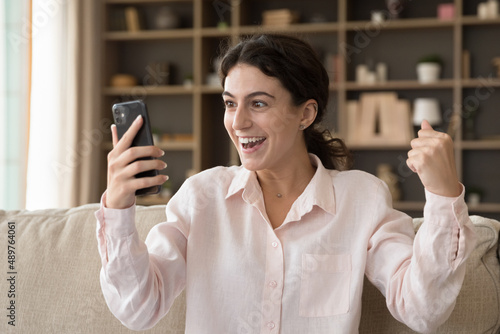 Overjoyed surprised young Hispanic woman making yes gesture looking at smartphone screen, feeling excited reading message with online lottery gambling giveaway win notification, internet success.