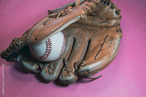 Baseball resting in a baseball mitt, glove, with a pink background. 
