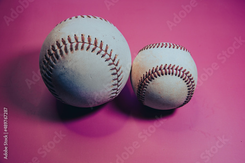 Softball next to a Baseball with a pink background.