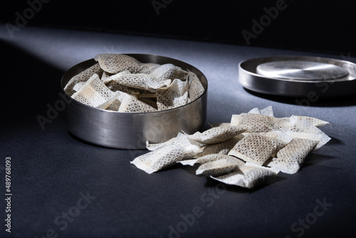 Closeup of metallic Swedish snus can with white portions of smokeless tobacco pouches against a dark background.