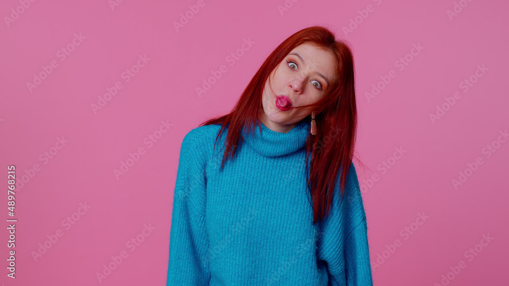 Funny comic teen student girl 20s years old in blue sweater making playful silly facial expressions and grimacing, fooling around showing tongue. Young adult woman isolated on pink wall background Funny comic teen student girl 20s years old in blue sweater making playful silly facial expressions and grimacing, fooling around showing tongue. Young adult woman isolated on pink wall background