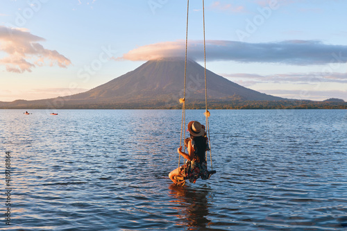 Back view of woman sitting on a swing overlooking the volcano concenpcion on ometepe island, Nicaragua.