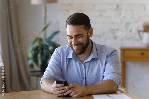 Handsome businessman sits at table holds in hands smart phone enjoy on-line chat, share messages through messenger or social media, distracted from work use modern tech, internet connection concept