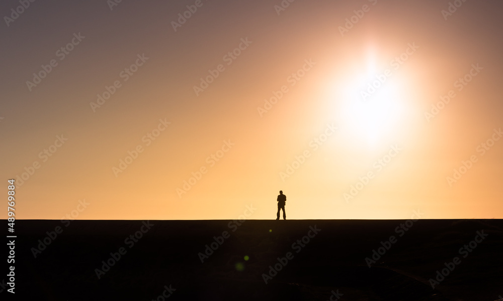 Silhouette of man from a far distance facing the morning sunrise 