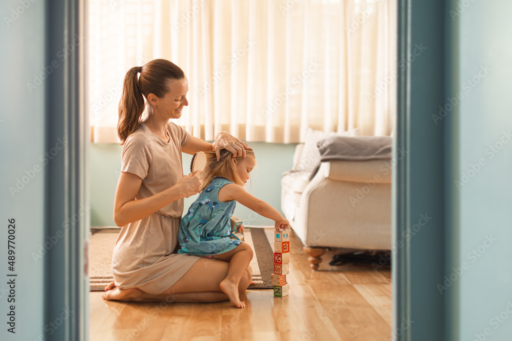 Mother taking care of her daughter child at home brushing her hair. Child care and parenting concept Mother taking care of her daughter child at home brushing her hair. Child care and parenting concept