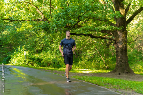 A man athlete runs in the park outdoors, around the forest, oak trees green grass young enduring athletic athlete athlete fitness legs jog, trees man. Adult running, morning stretches