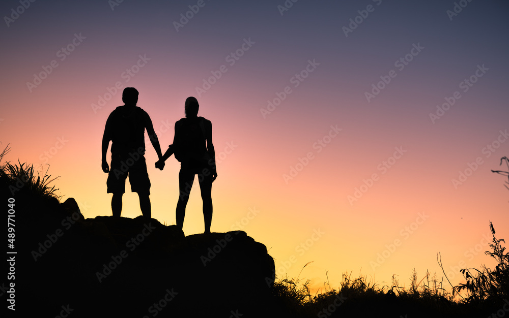 Couple hikers man and woman holding hands on top of a mountain looking out to the sunset view. Unity and togetherness concept 