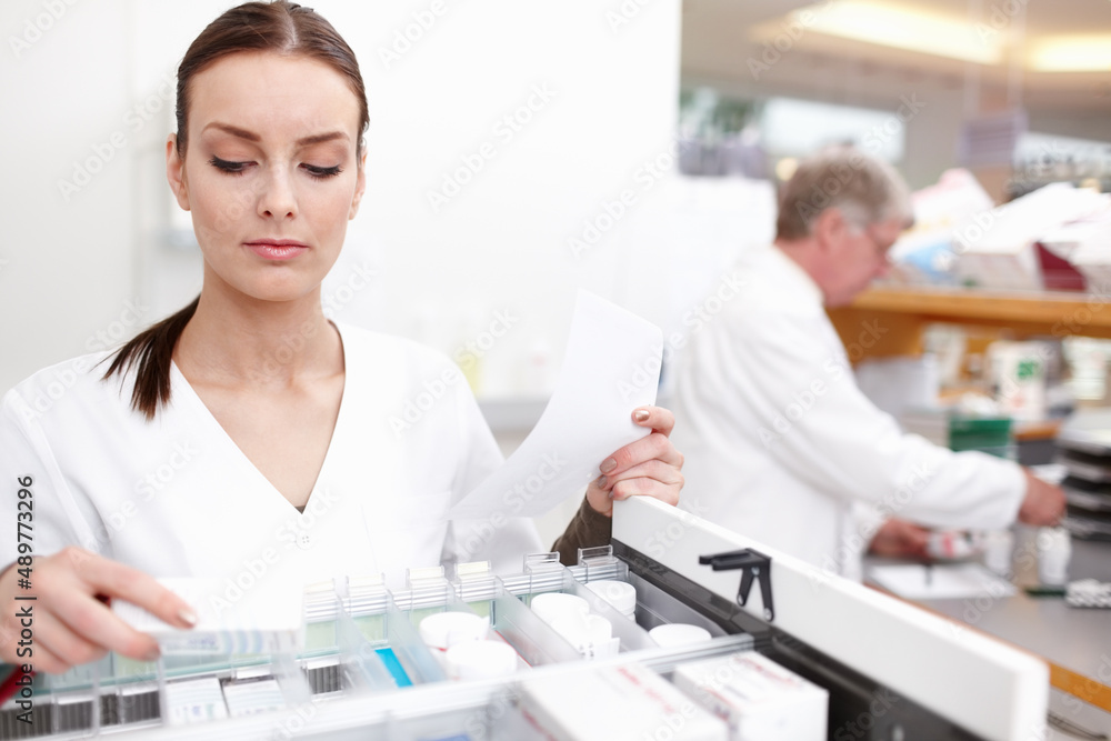 Pharmacist checking medicines with colleague. Portrait of female pharmacist checking medicines with colleague working in background. Pharmacist checking medicines with colleague. Portrait of female pharmacist checking medicines with colleague working in background.