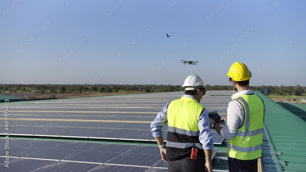 Professional engineer using drone and digital tablet maintaining solar cell panels together on building rooftop. Technician working on ecological solar farm. Renewable clean energy technology concept Professional engineer using drone and digital tablet maintaining solar cell panels together on building rooftop. Technician working on ecological solar farm. Renewable clean energy technology concept
