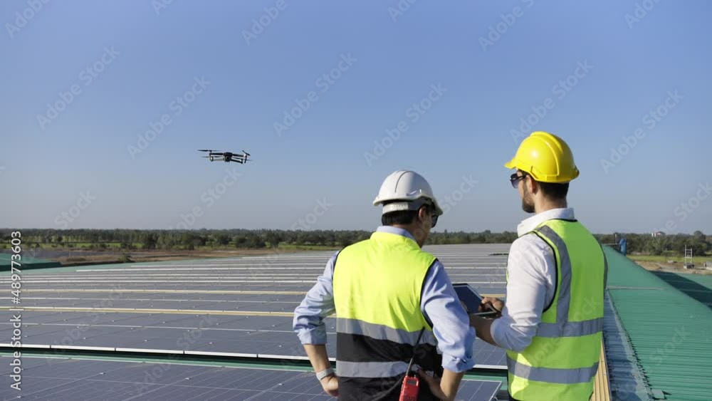 Professional engineer using drone and digital tablet maintaining solar cell panels together on building rooftop. Technician working on ecological solar farm. Renewable clean energy technology concept Professional engineer using drone and digital tablet maintaining solar cell panels together on building rooftop. Technician working on ecological solar farm. Renewable clean energy technology concept