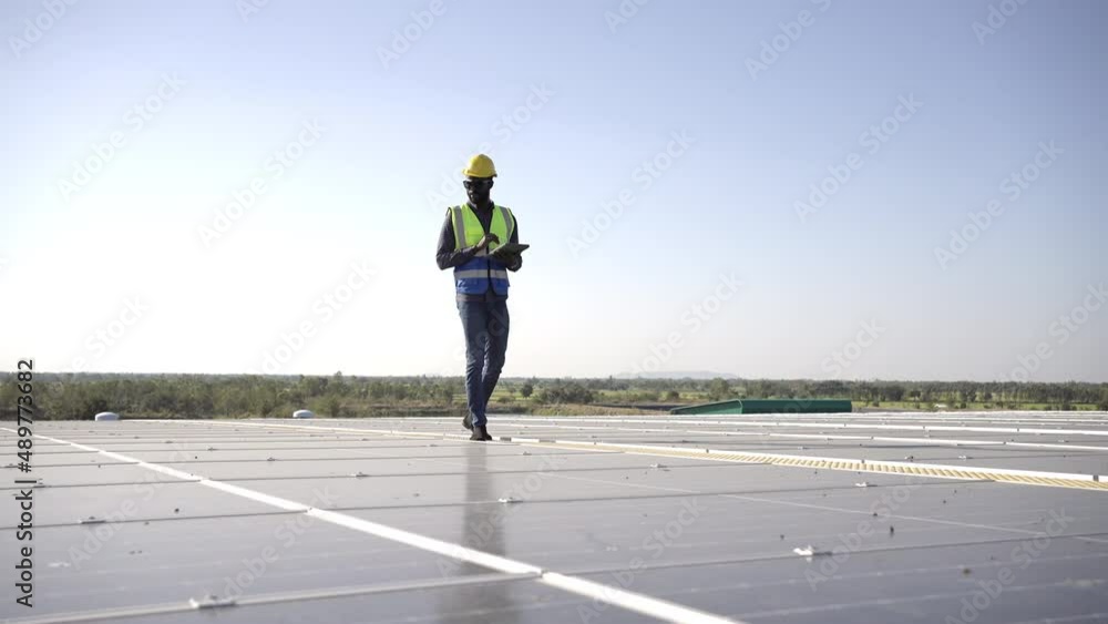 African man engineer using digital tablet maintaining solar cell panels on building rooftop. Technician working outdoor on ecological solar farm construction. Renewable clean energy technology concept African man engineer using digital tablet maintaining solar cell panels on building rooftop. Technician working outdoor on ecological solar farm construction. Renewable clean energy technology concept