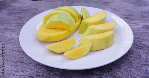 Ripe mango slices on a white plate Placed on an old wooden floor, food and fruit are high in vitamins for good health.