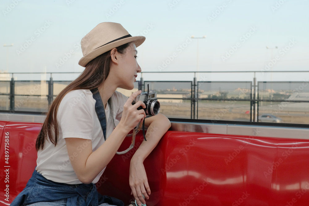 Beautiful Asian female tourist sits in a red seat, traveling by train, taking snapshot photo, transporting in suburb view, enjoy passenger lifestyle by railway, happy journey vacation.