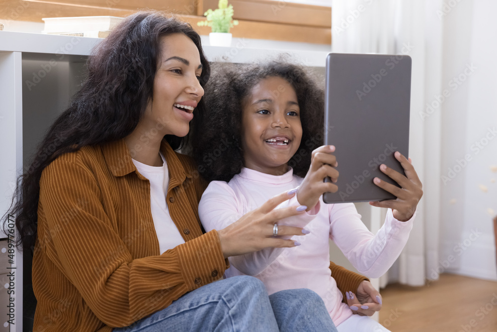 Happy two female generations African American family using digital touchpad gadget, holding web camera call conversation, watching funny video online, choosing goods shopping in internet store. Happy two female generations African American family using digital touchpad gadget, holding web camera call conversation, watching funny video online, choosing goods shopping in internet store.