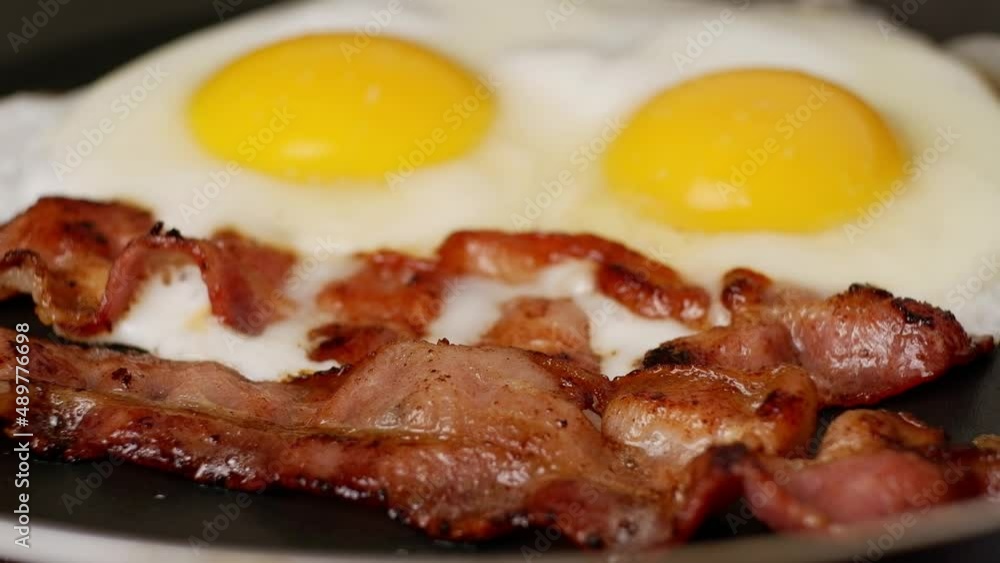 Two pieces of fried crispy bacon and fried eggs with on a hot pan. Two pieces of fried crispy bacon and fried eggs with on a hot pan.