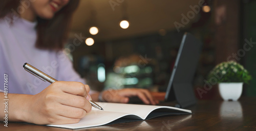 Closeup image of woman using pen writing on notebook or paper report in office.