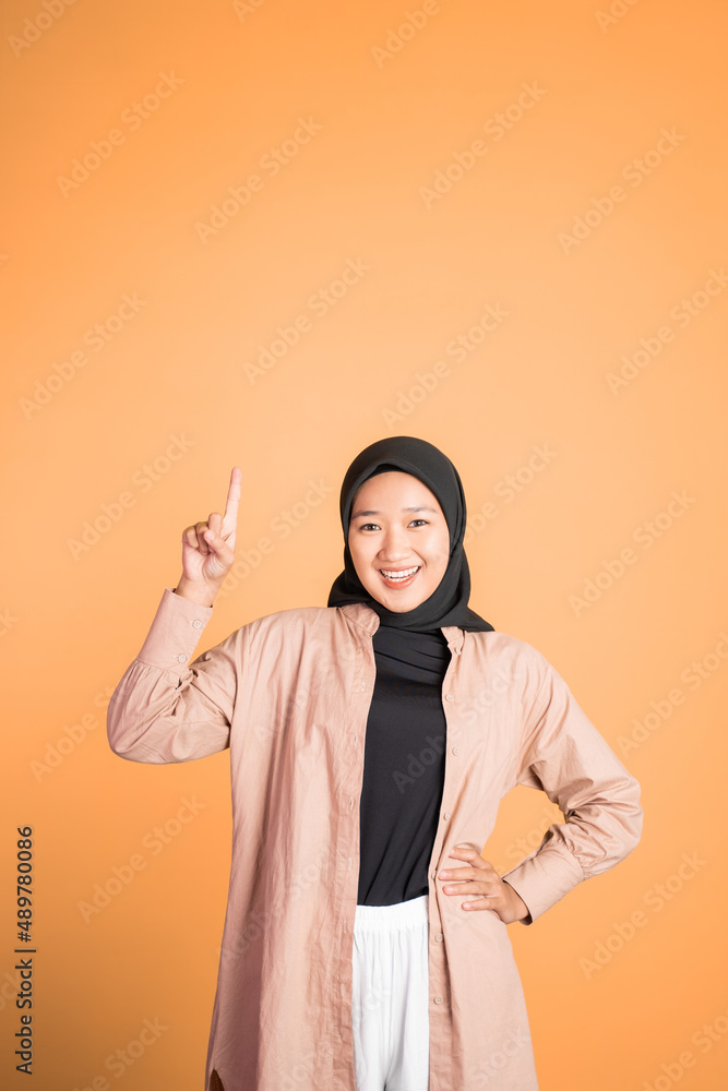 Smiling hijab woman with finger pointing up hand gesture Smiling hijab woman with finger pointing up hand gesture