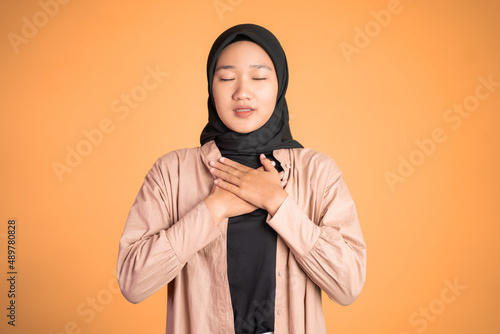 muslim woman close eyes holding chest while feeling relieved
