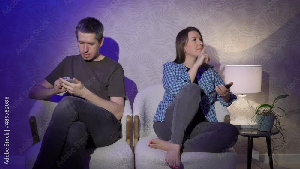 Man and woman sits on an armchair and using mobile phone in the evening at home. Man and woman sits on an armchair and using mobile phone in the evening at home.