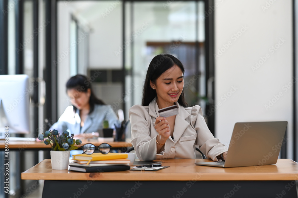 Happy young female office worker holding credit car and shopping online on laptop computer. Happy young female office worker holding credit car and shopping online on laptop computer.