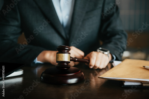 Close up view of auction hammer on the desk in lawyer office and lawyer writing document as courtroom.