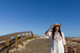 Mujer latina. Señora, adulta con gafas de sol, sombrero y  vestida de blanco, sobre  un puente de madera en la playa.
