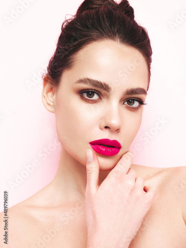 Fashion beauty portrait of young brunette woman with evening stylish  makeup and perfect clean skin. Sexy model with hair in a bun posing in studio near white wall. With pink bright natural lips