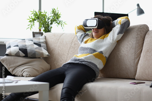 Female lay casually on couch in vr glasses, use modern device at home, test new development photo