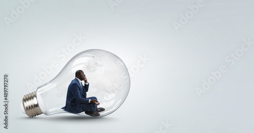Young black man sitting and meditating inside light bulb