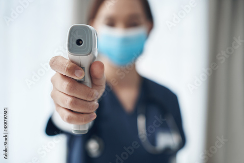 Temperature checks are important during this pandemic. Shot of a young female doctor pointing a thermometer in an office.