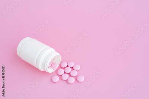 Pink pills on pink background, white plastic bottle, medical tablets, pills, vitamins for woman, health, wellness, recuperate, space for text