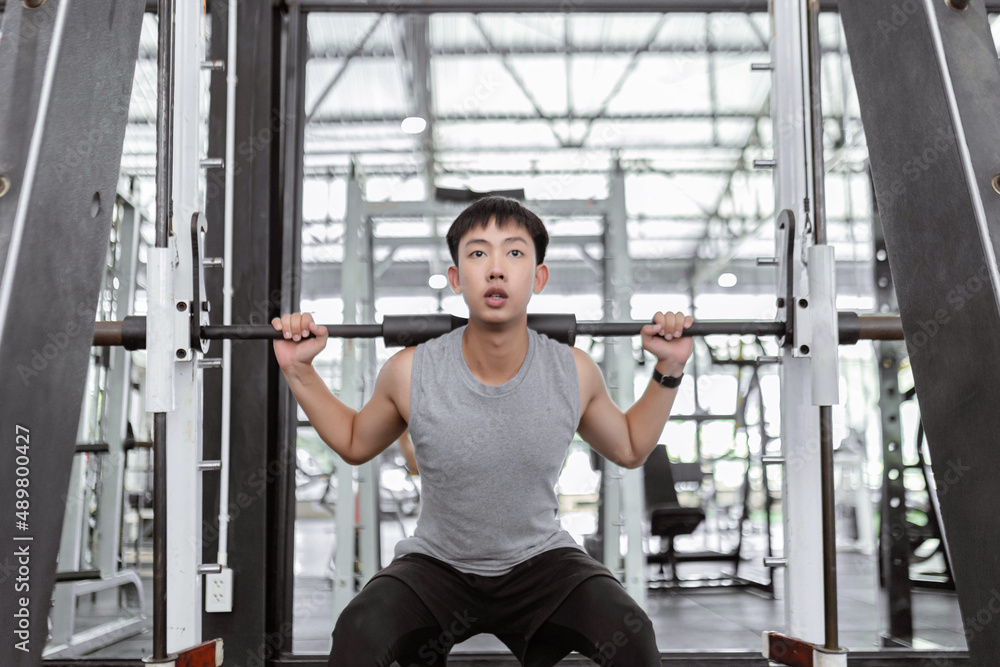 exercise concept The strong guy playing weight machine by carrying the weight on his shoulders and sitting into a squat position exercise concept The strong guy playing weight machine by carrying the weight on his shoulders and sitting into a squat position