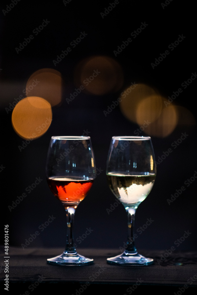 Two backlit and partially filled wine glasses with red and white wine sitting on a bar with twilight bokeh. Two backlit and partially filled wine glasses with red and white wine sitting on a bar with twilight bokeh.