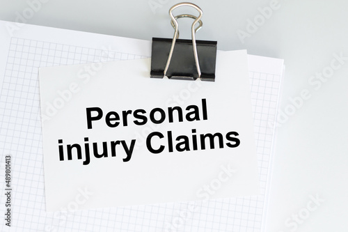 text PERSONAL INJURY CLAIMS on a card clip to a notepad on a white table, business