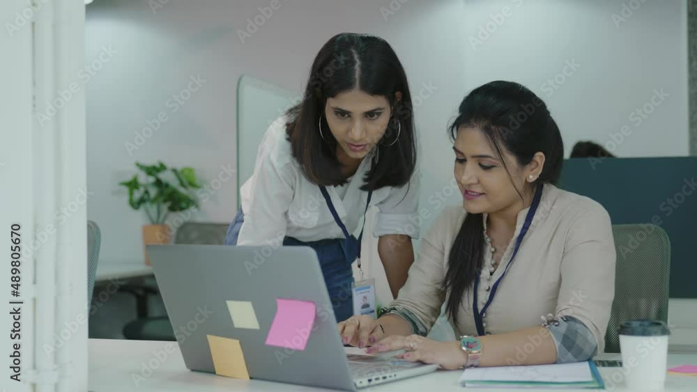 Two Indian young and attractive office female employees,workers working together on a laptop in a modern office.two diverse female employees corporate in co-working workplace with laptop. Two Indian young and attractive office female employees,workers working together on a laptop in a modern office.two diverse female employees corporate in co-working workplace with laptop.