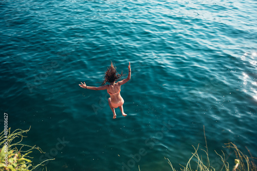 Woman jumping off cliff into the sea. Summer fun lifestyle.