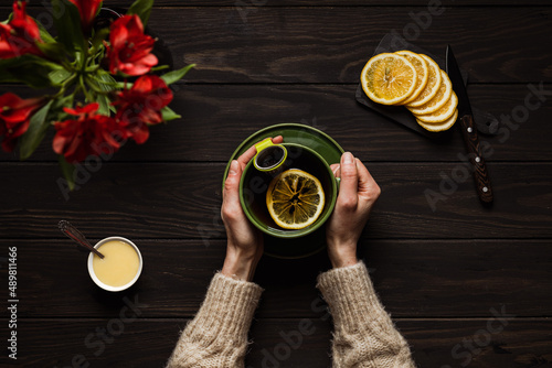 Woman in a cozy beige sweater drinking a big cup of hot tea with lemon and honey, on wooden background, overhead shot
