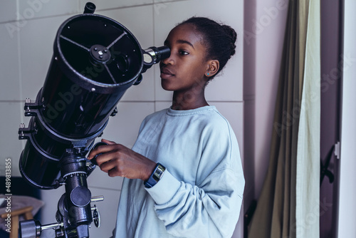 Pre-adolescent girl looking through telescope at home photo