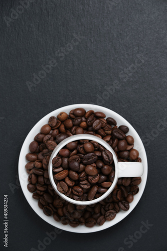 Fragrant coffee beans in a white coffee cup top view. Coffee beans on black slate copy space. Coffee beans in a cup on a black background flat lay.