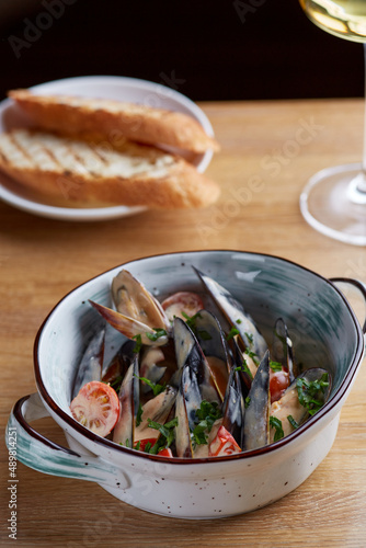 mussels with sauce and grilled bread in plate on wooden table with glass of white wine near and dark background. restaurant concept