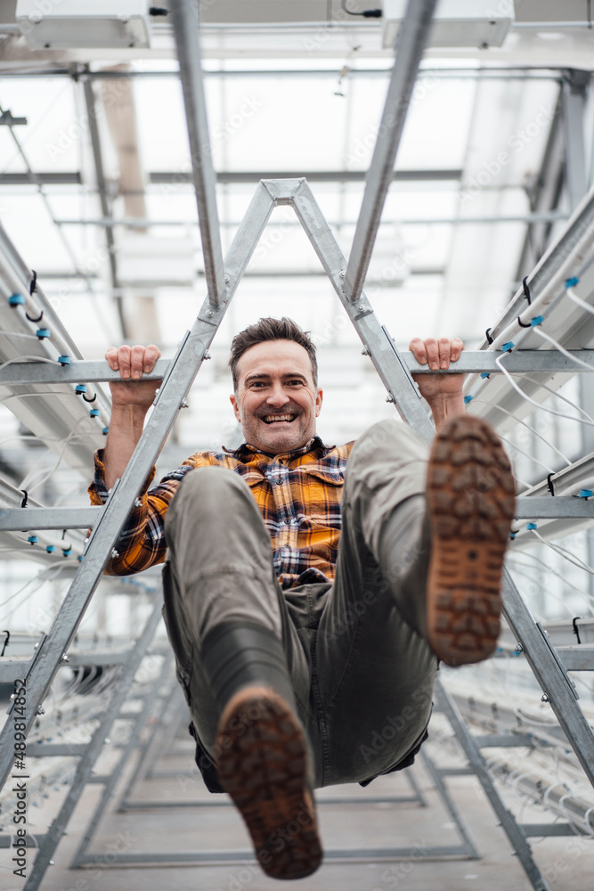 Cheerful employee swinging on rack in greenhouse Cheerful employee swinging on rack in greenhouse