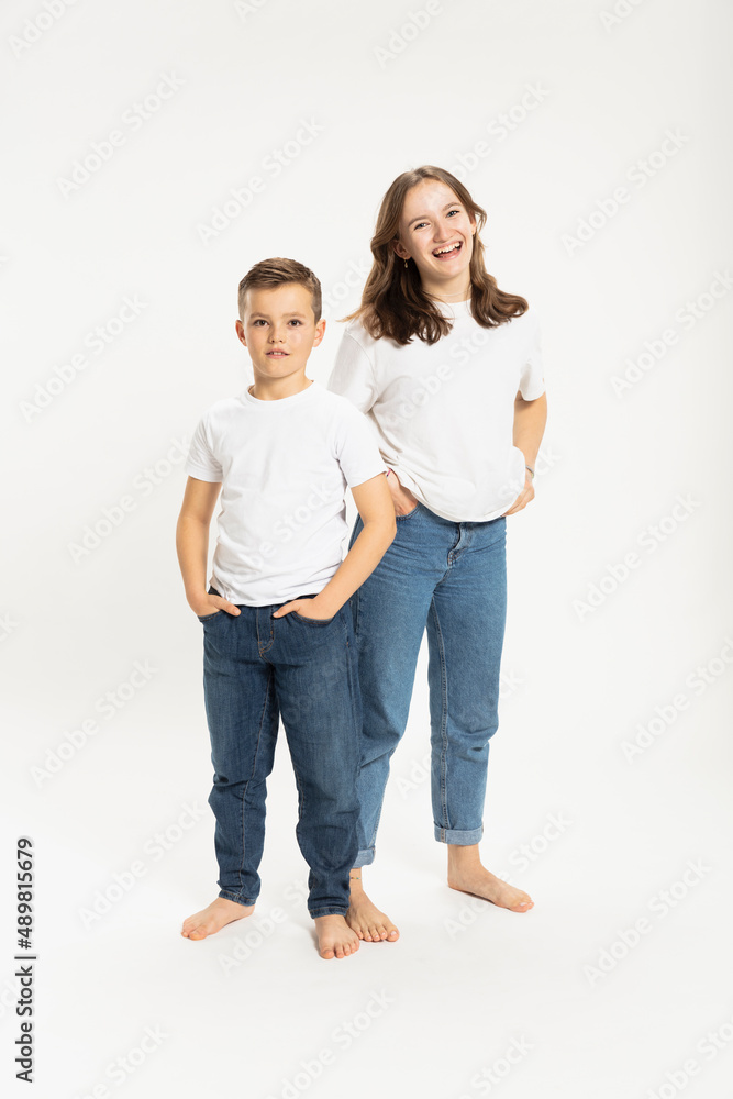 Happy girl and brother standing with hands in pockets against white background Happy girl and brother standing with hands in pockets against white background