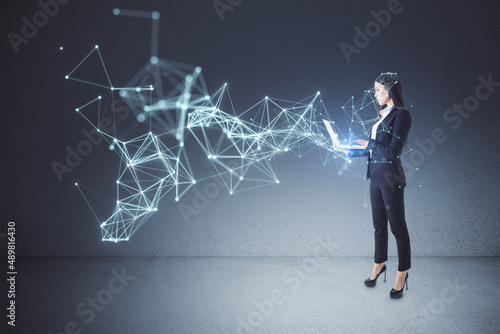 Attractive young european businesswoman with laptop using abstract polygonal network mesh hologram in concrete interior. Metaverse and AI concept. © Who is Danny