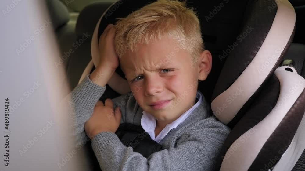 Portrait of a tired little boy in a shirt and jumper with a backpack in the car in the back seat, holding his head with his hands. Portrait of a tired little boy in a shirt and jumper with a backpack in the car in the back seat, holding his head with his hands.