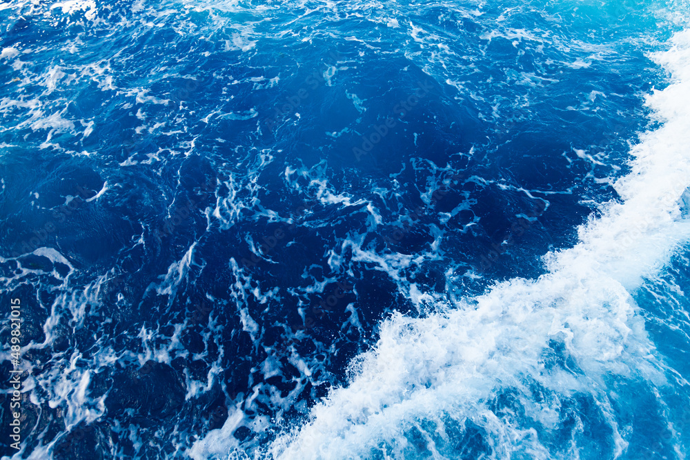 Rolling waves in the ocean. Blue water background with white foam. Rushing water in the open sea.