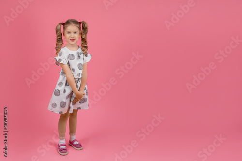 a little girl in a beautiful dress with curly tails on a solid pink background