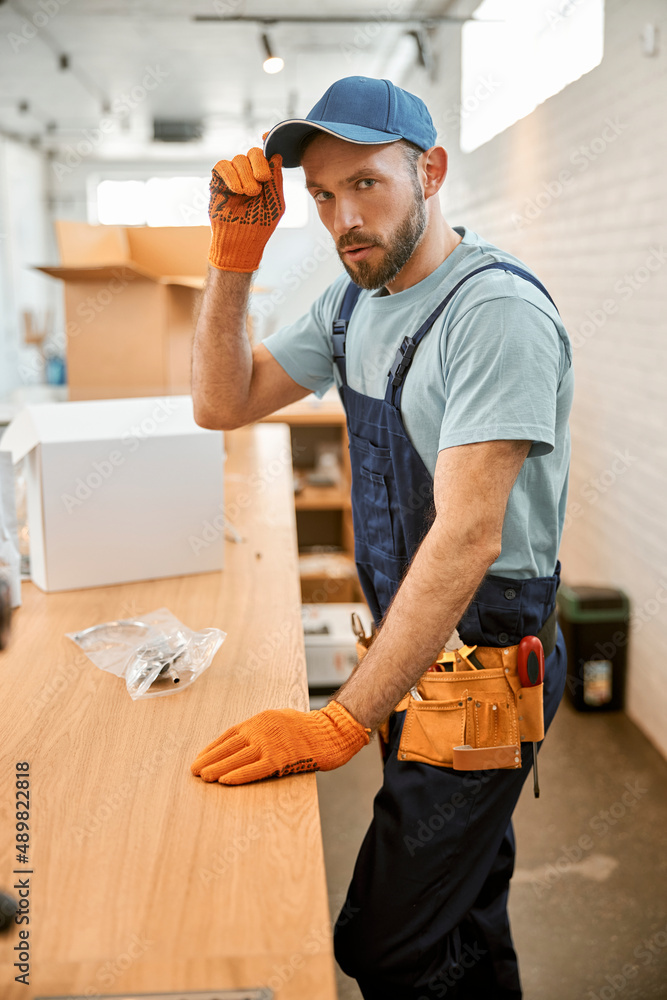 Bearded repairman in cap standing by the table Bearded repairman in cap standing by the table
