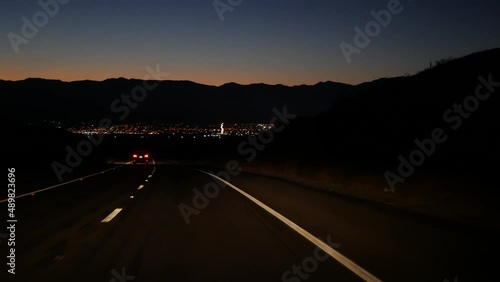 Car driving on desert road at night, freeway or highway in twilight dusk, perspective view thru windscreen or windshield. Road trip in California USA. Valley and mountains on horizon, dividing line.