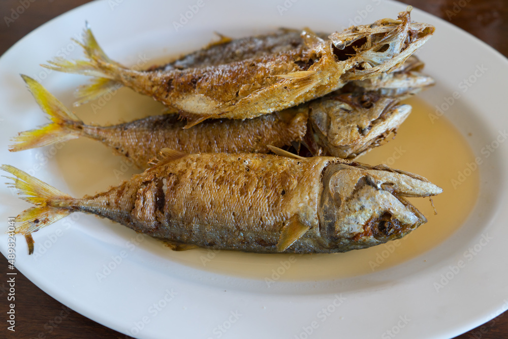 Fried mackeral fish with sour sauce for health food on white plate. Delicious Thai food on wooden table background. Fried mackeral fish with sour sauce for health food on white plate. Delicious Thai food on wooden table background.