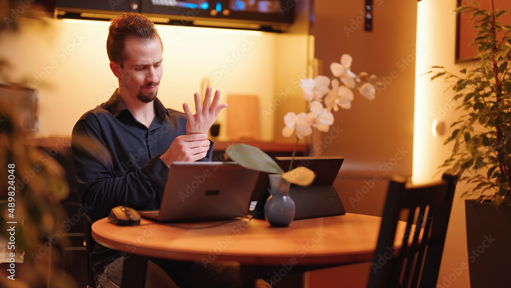 Male person behind laptop computer in kitchen with wrists pain problems work at home Male person behind laptop computer in kitchen with wrists pain problems work at home
